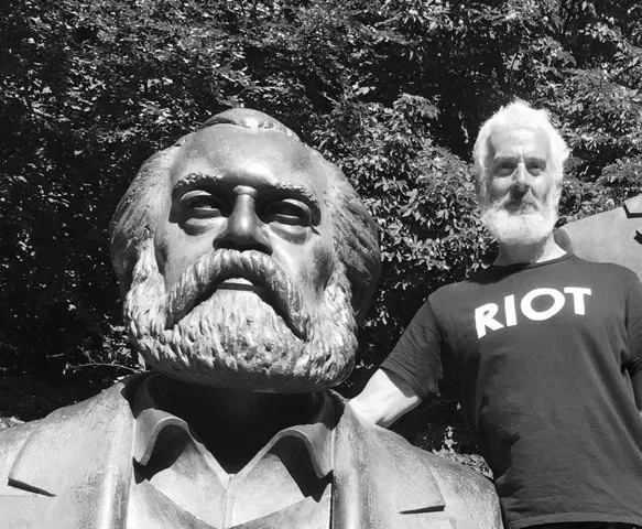 A black and white photo of a man standing next to a statue of a man with a beard.