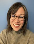A woman with glasses wearing a sweater smiles at the camera.