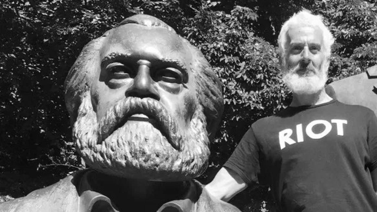 A black and white photo of a man standing next to a statue of a man with a beard.