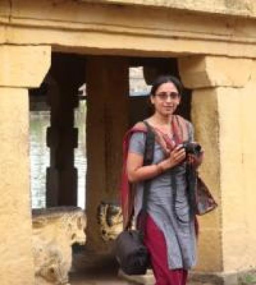 Professor Venkatesan, holding a camera and looking at the viewer while standing in front of a point of interest.