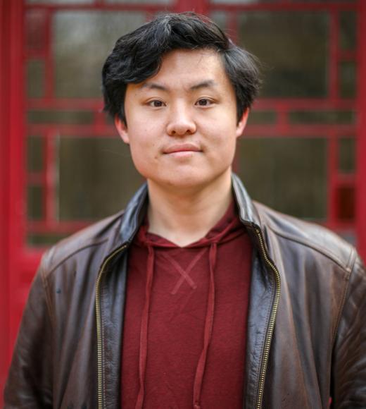 Man in black jacket in front of red and brown fuzzy background.