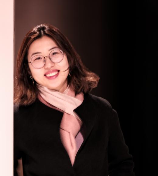 A woman with glasses leaning against a white post smiling at the camera