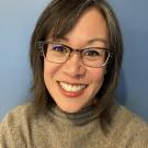A woman with glasses wearing a sweater smiles at the camera.