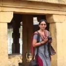 Professor Venkatesan, holding a camera and looking at the viewer while standing in front of a point of interest.