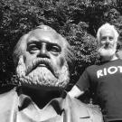 A black and white photo of a man standing next to a statue of a man with a beard.