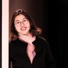 A woman with glasses leaning against a white post smiling at the camera